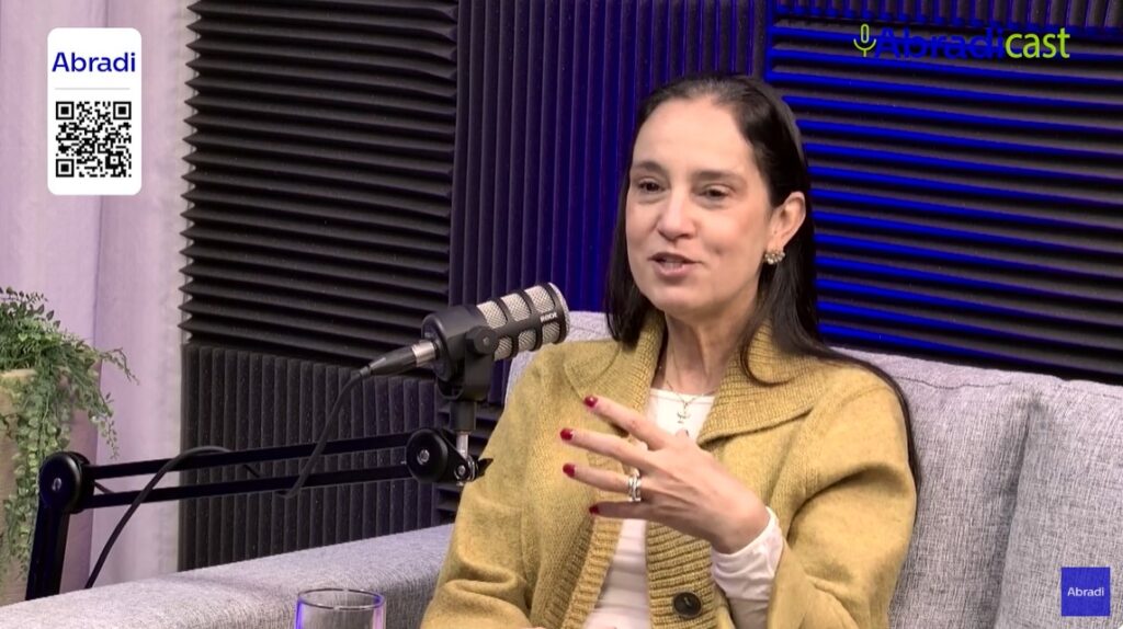 Imagem Fabia Juliasz mulher branca de cabelos negros vestindo tailleur mostarda, conselheira ABAP falando no Abradicast sobre a pesquisa Por Dentro das Agências